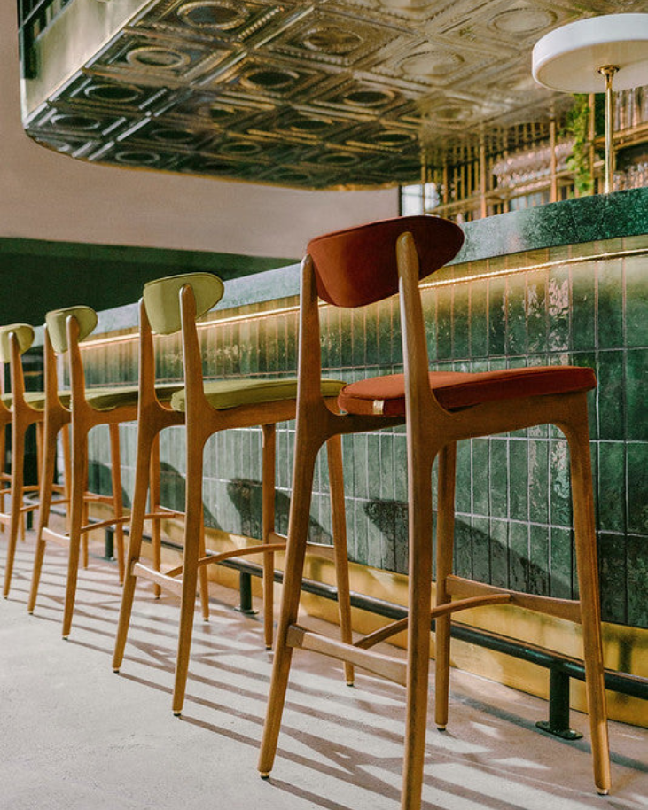 Row of wooden bar stools in a bar setting with decorative ceiling.